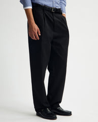 Zwarte geplooide regular fit broek aan model, rechte pijpen, plooien en riemlussen.