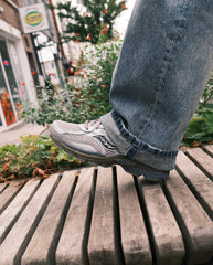 Saucony sneaker lichtgrijs naast blauwe jeans; veters, geperforeerd bovenwerk en dikke zool