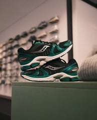 Saucony hardloopschoenen in zwart en donkergroen, zijaanzicht op platform