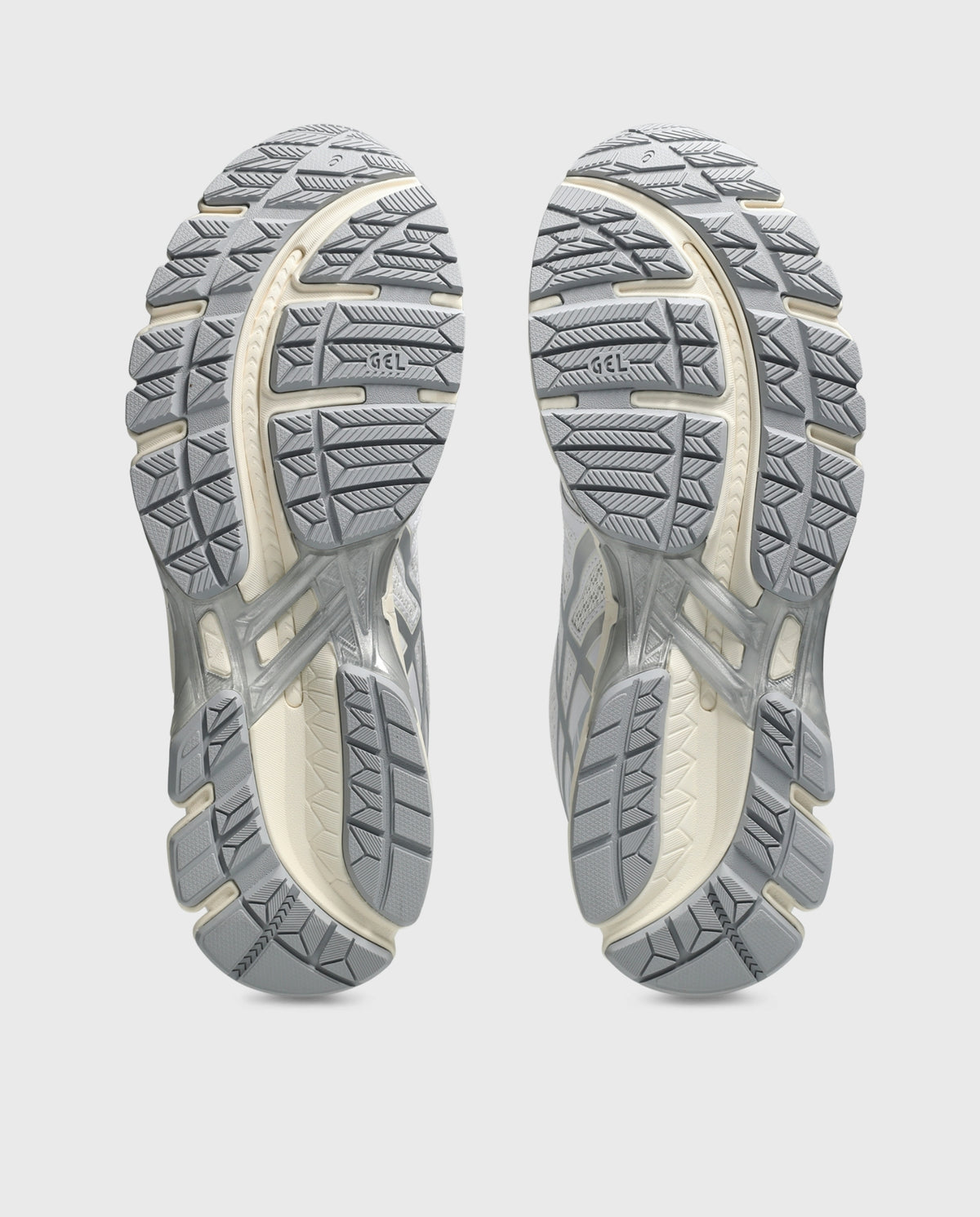 Paar Asics hardloopschoenen met grijze profielzolen, onderzichten op grondefffect.