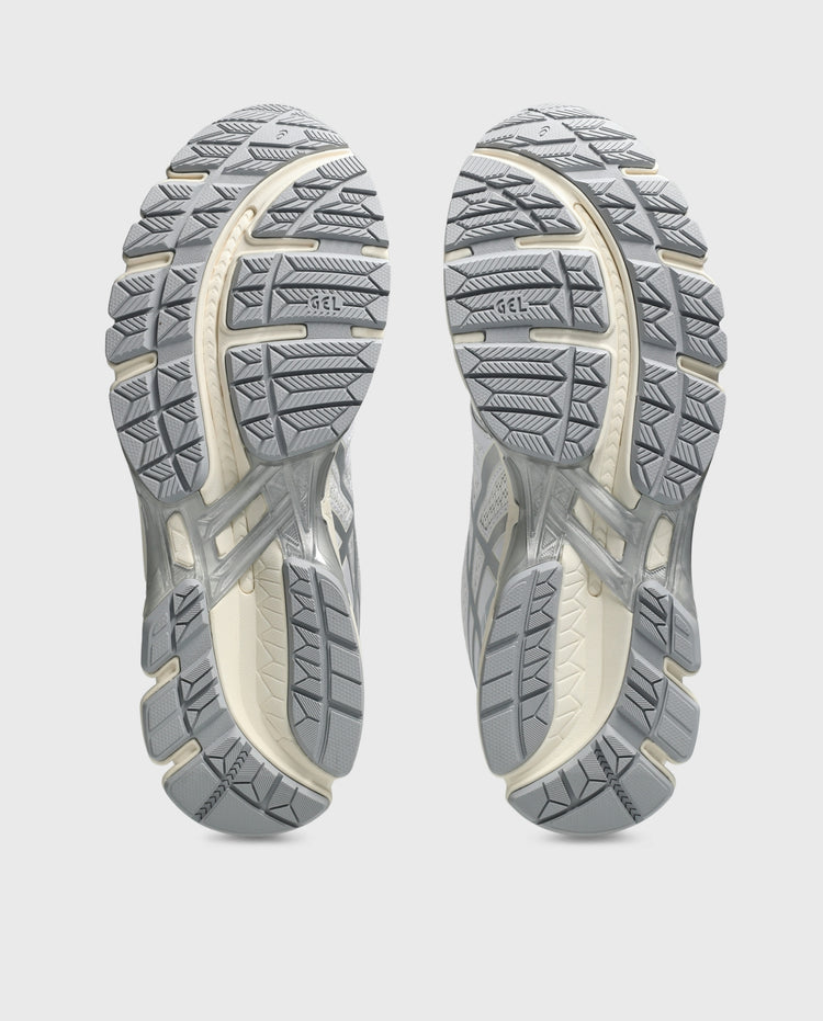 Paar Asics hardloopschoenen met grijze profielzolen, onderzichten op grondefffect.