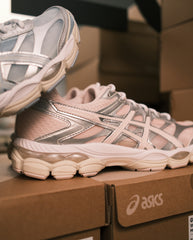 Asics hardloopschoen in lichtroze en zilver, zichtbare zijpanelen en vetersluiting.