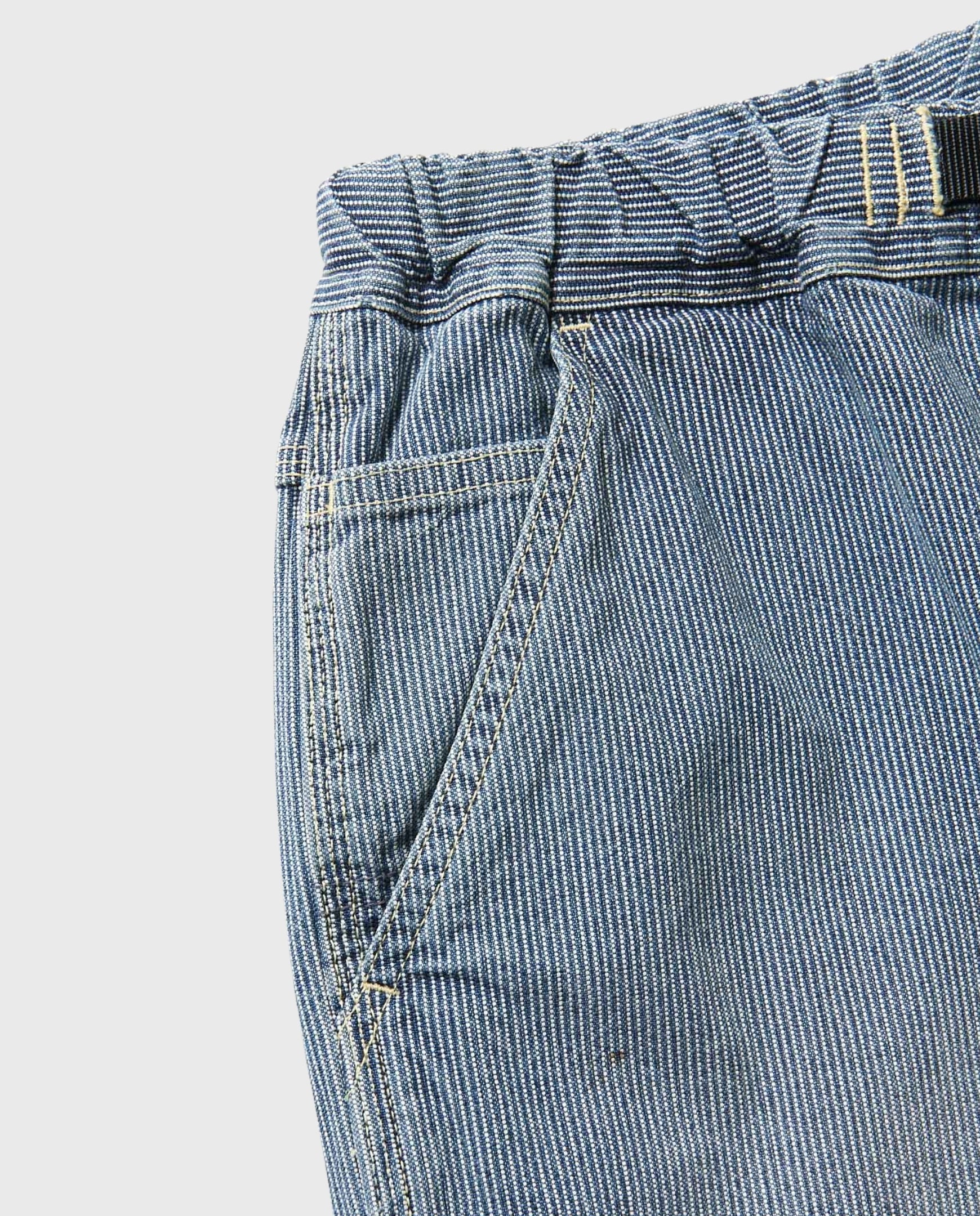 Detail van voorzijde denim werksbroek met opgestikte zak en elastische taille