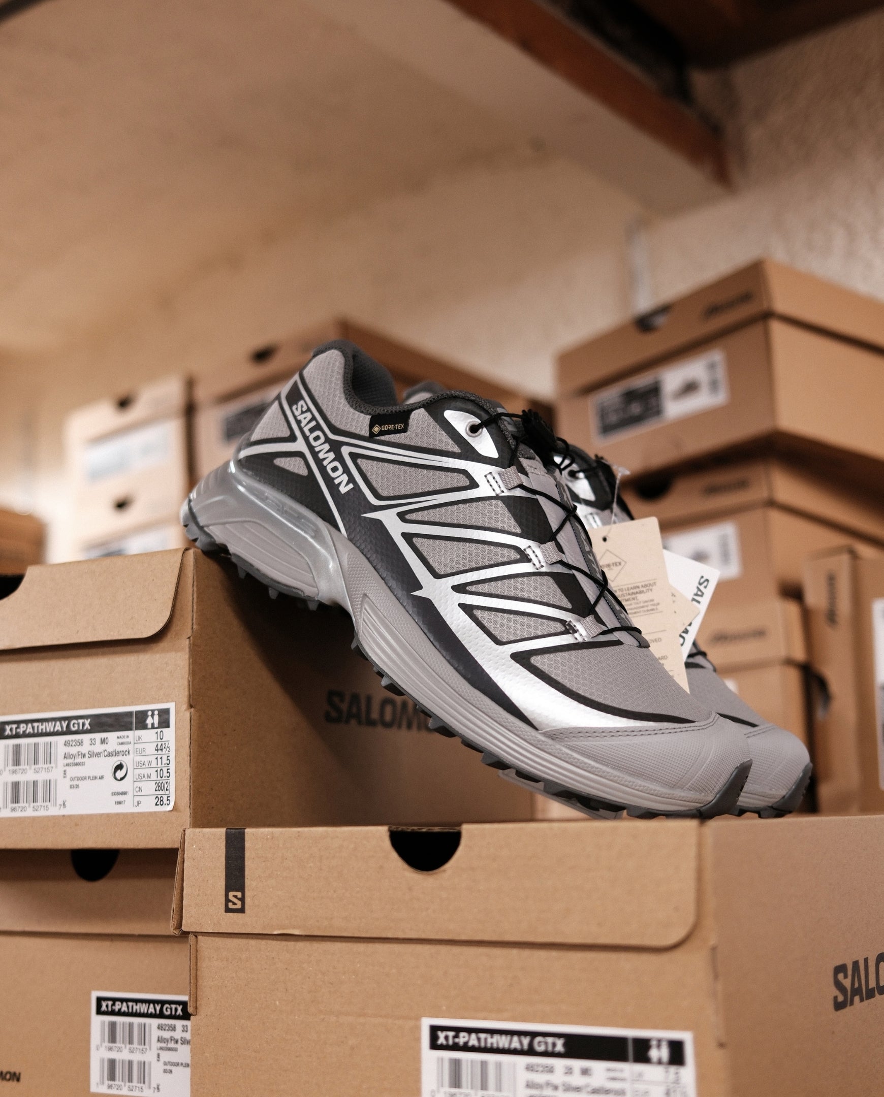Salomon trailhardloopschoen zilvergrijs met zwarte veters, op kartonnen dozen