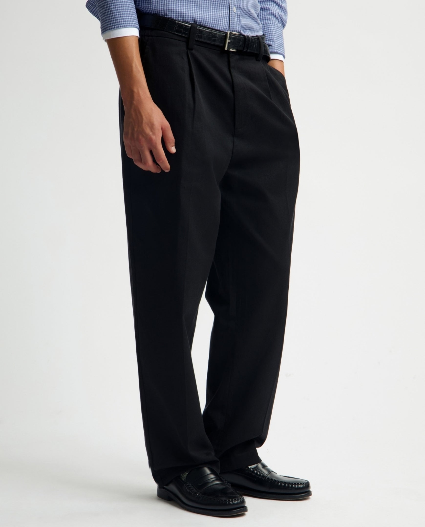 Zwarte geplooide regular fit broek aan model, rechte pijpen, plooien en riemlussen.