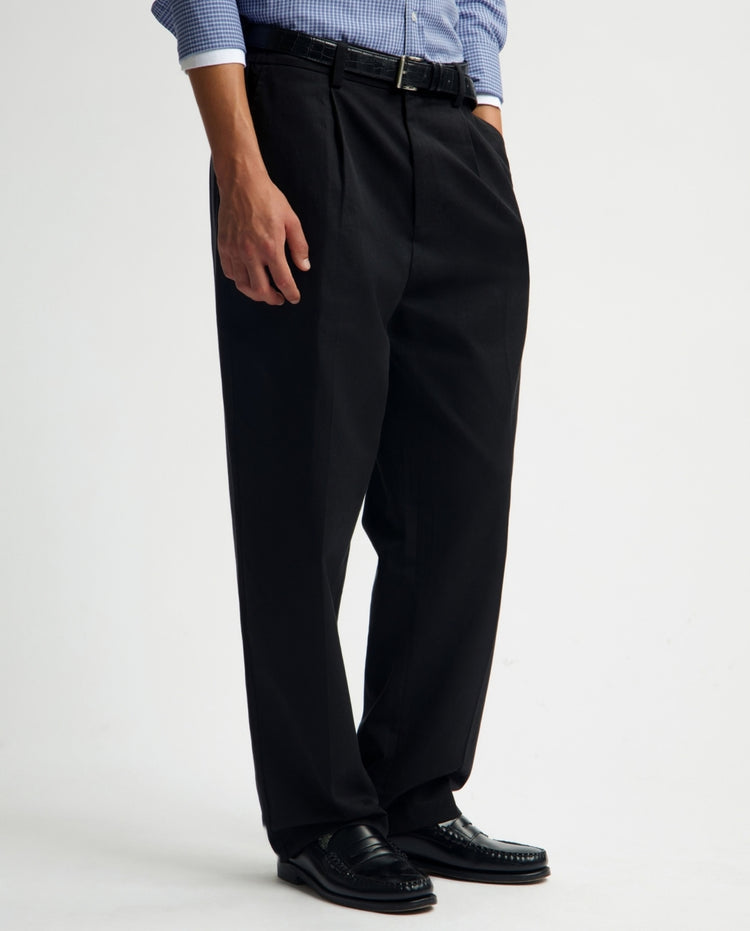 Zwarte geplooide regular fit broek aan model, rechte pijpen, plooien en riemlussen.