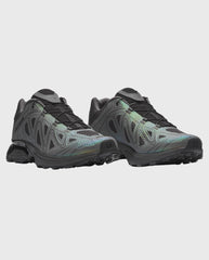Trailrunnerschoen met grijs-zwarte bovenkant en groene accenten, vetersluiting.