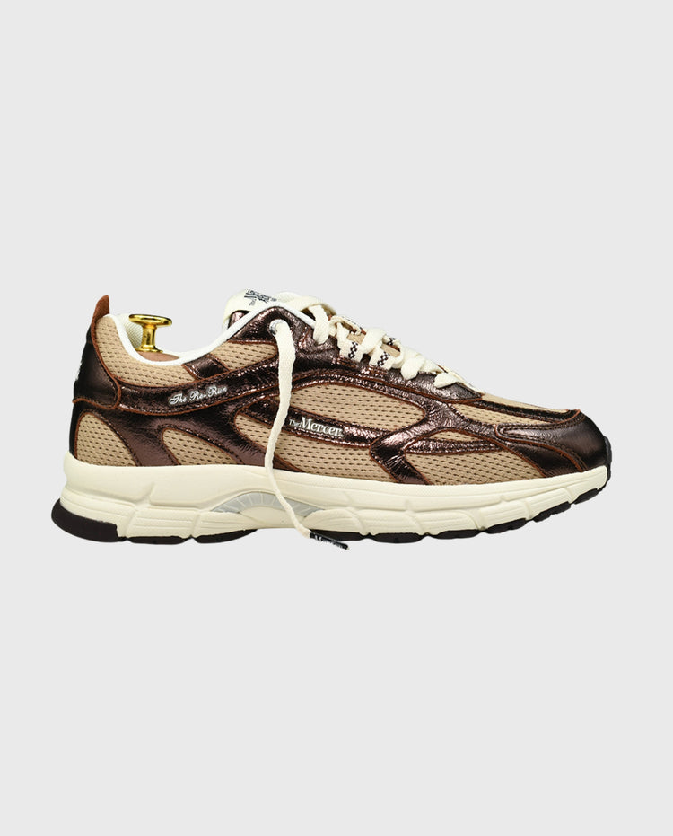 Bruin-beige sneaker met witte zool en gouden veteroog, zijaanzicht.