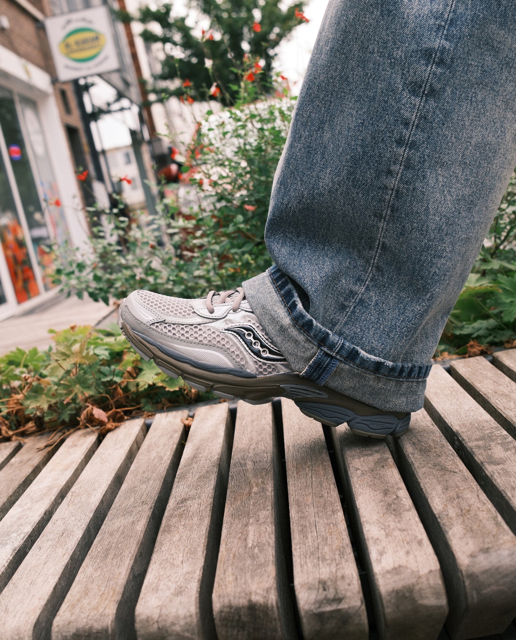 Saucony sneaker lichtgrijs naast blauwe jeans; veters, geperforeerd bovenwerk en dikke zool