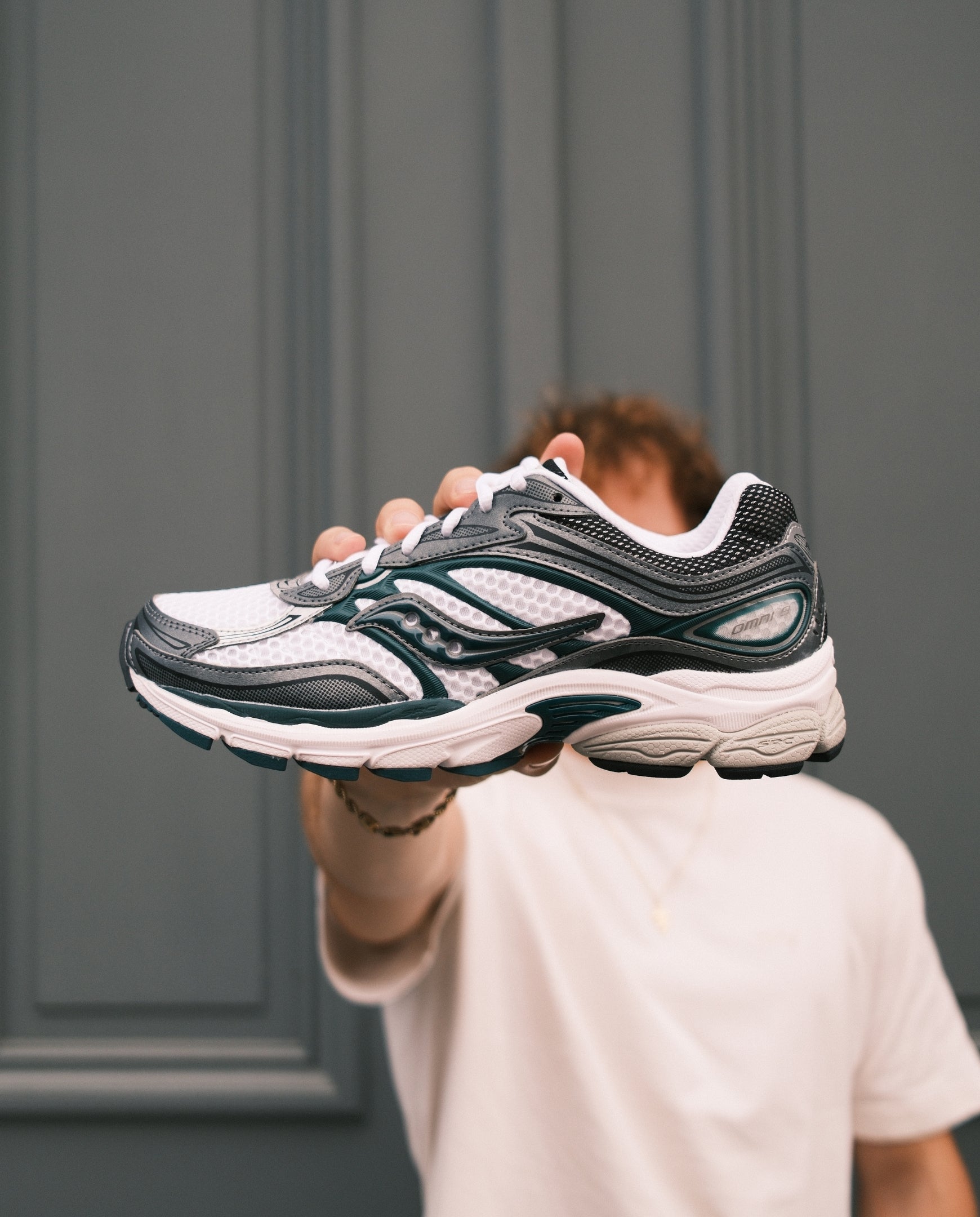 Saucony hardloopschoen met wit-grijze bovenkant, zwarte en groene details en dikke witte zool