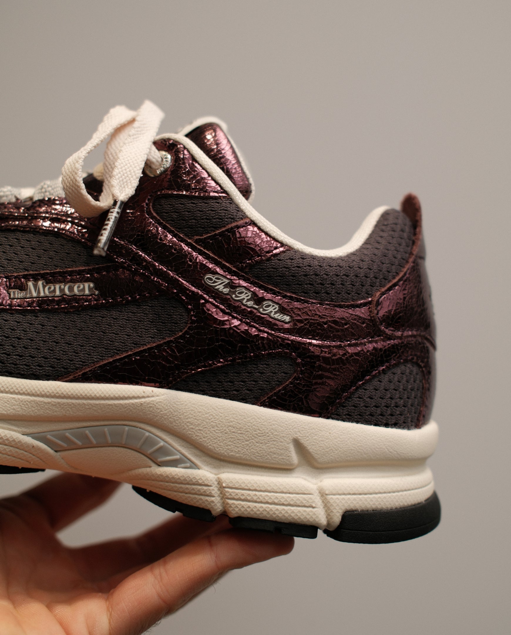 Donkerrode sneaker-detail met gebarsten textuur, witte veters en crèmezool