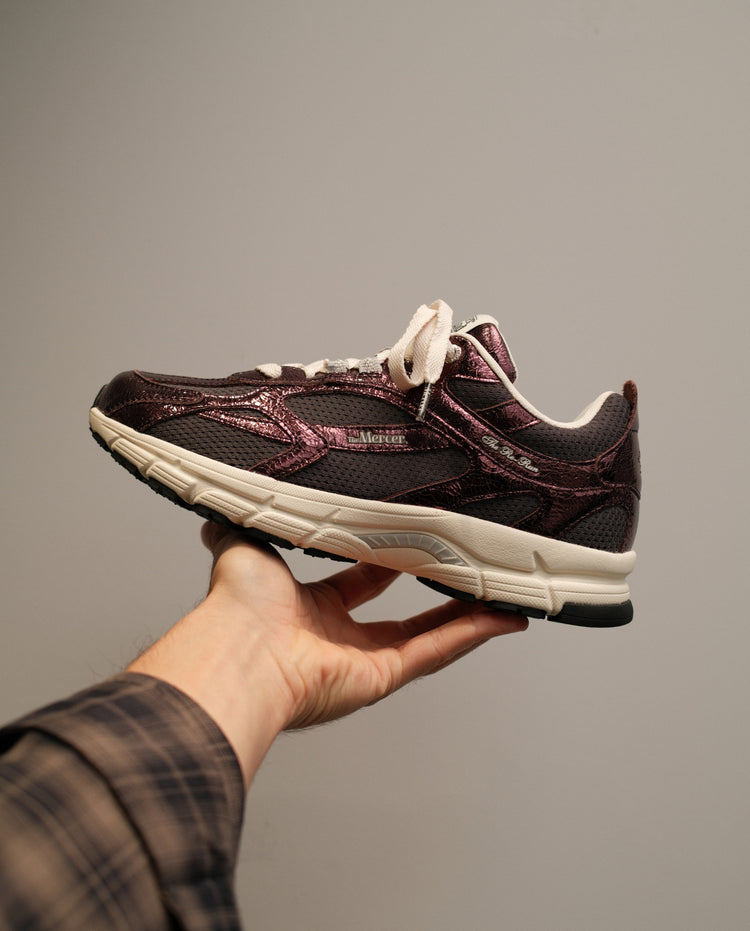 Donkerrode sneaker in hand vastgehouden, witte veters en crèmekleurige zool