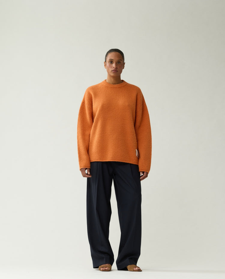 Oranje gebreide trui met ronde hals en lange mouwen; gedragen met donkere broek.