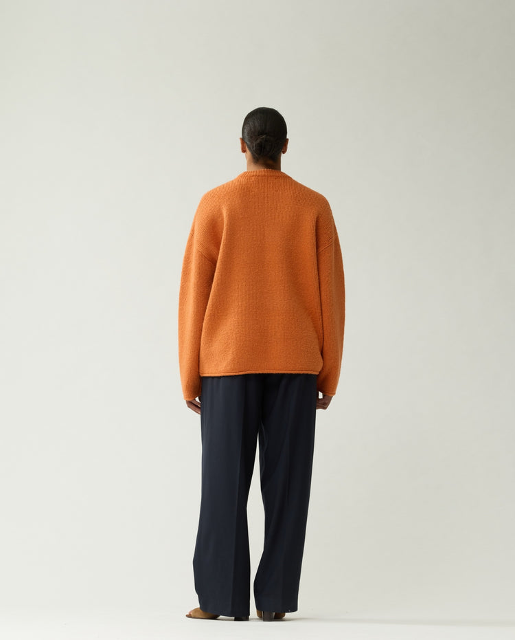Oranje gebreide trui met ronde hals en lange mouwen; rugaanzicht met donkere broek.