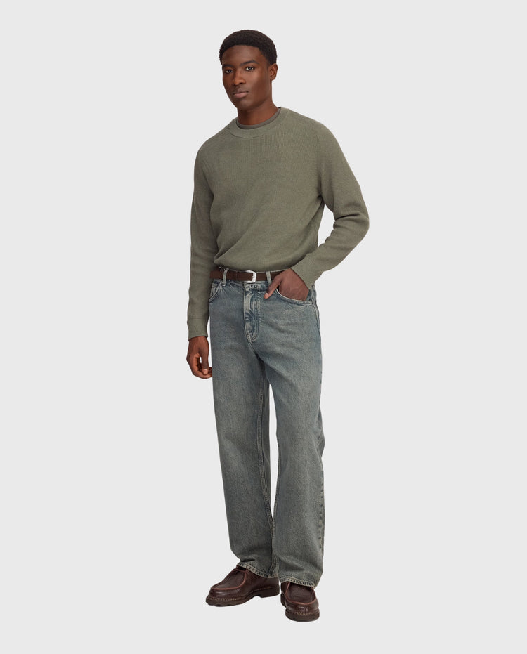 Blauwe stonewash jeans met rechte pijpen en riemlussen, gedragen met leren laarzen.